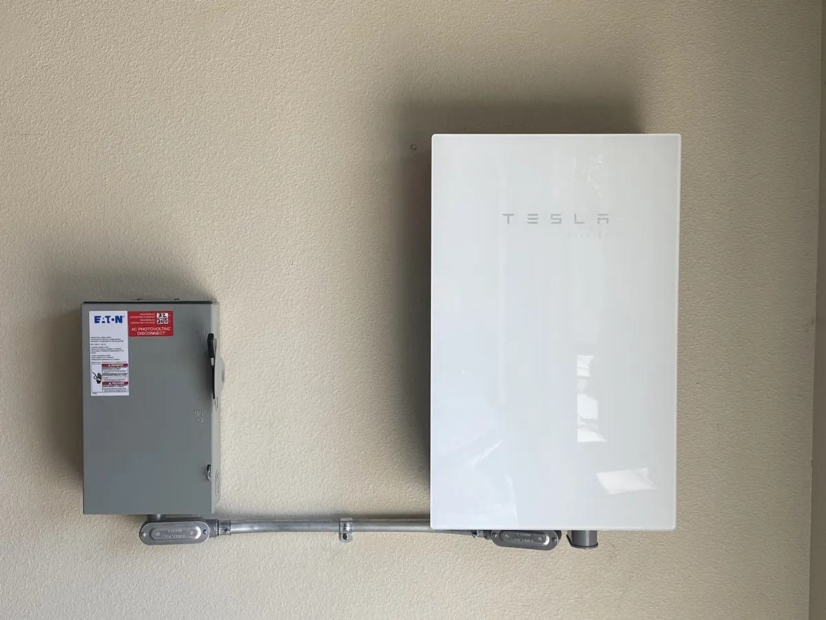 Inversor solar instalado na parede ao lado de uma chave seccionadora de corrente alternada